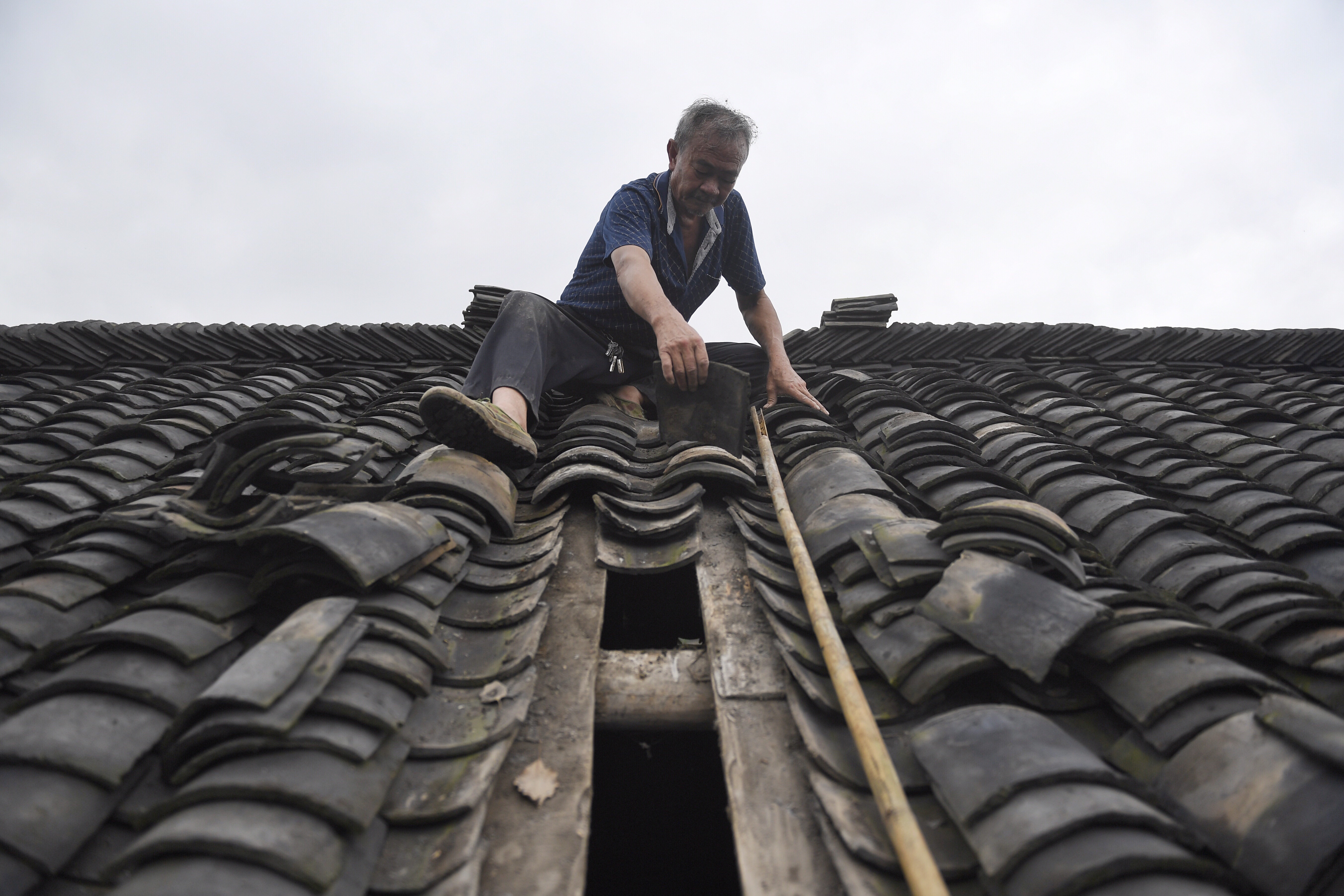 9月8日,威远县龙会镇新花村七组村民倪夕才在修补屋顶瓦片.